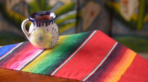 Ideas para decorar mesa mexicana para 15 de septiembre con mantel de colores a rayas y taza de barro